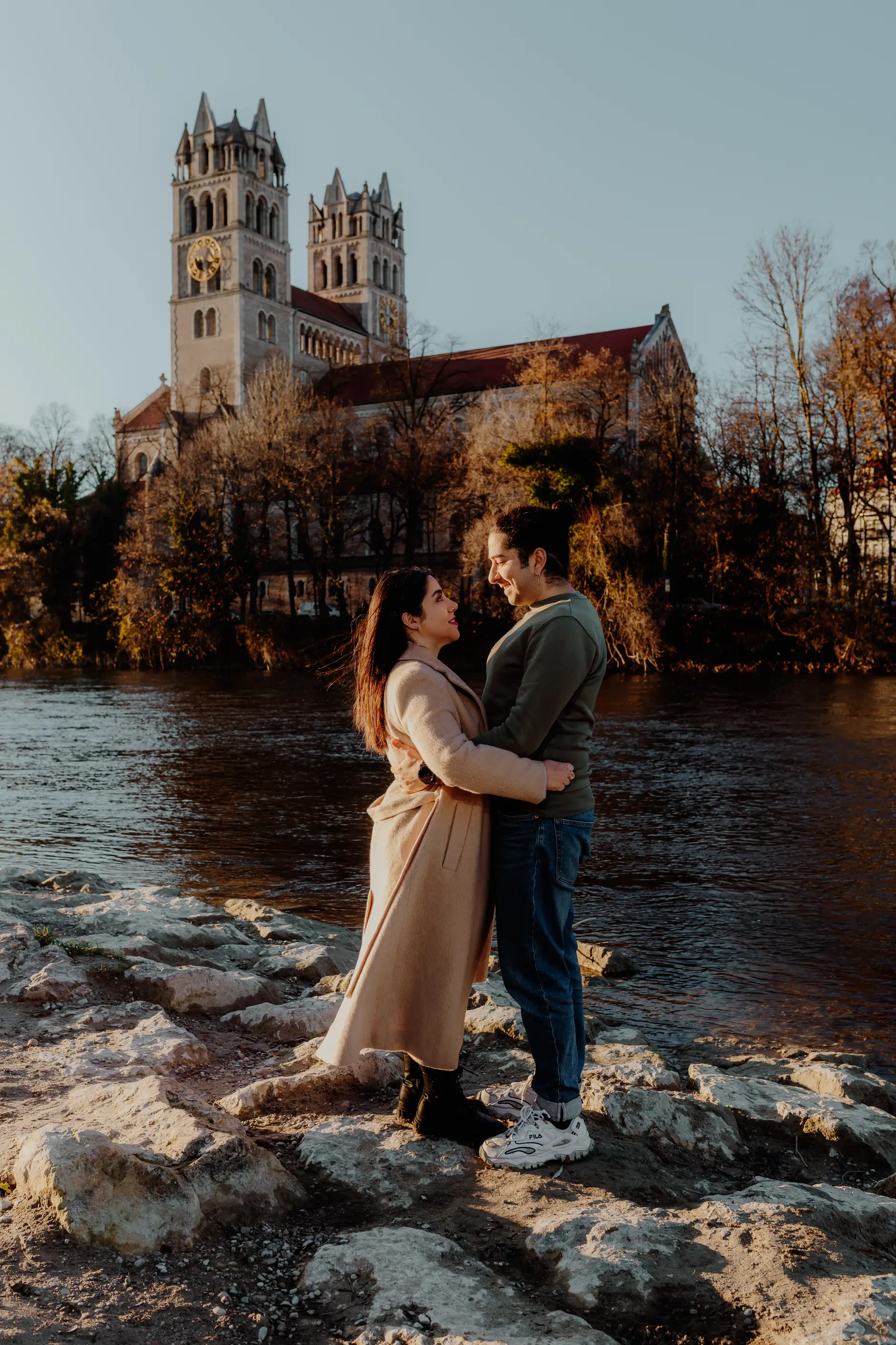 Couple on rocks at the Isar riverbank in Munich with a church in the background – couple photoshoot