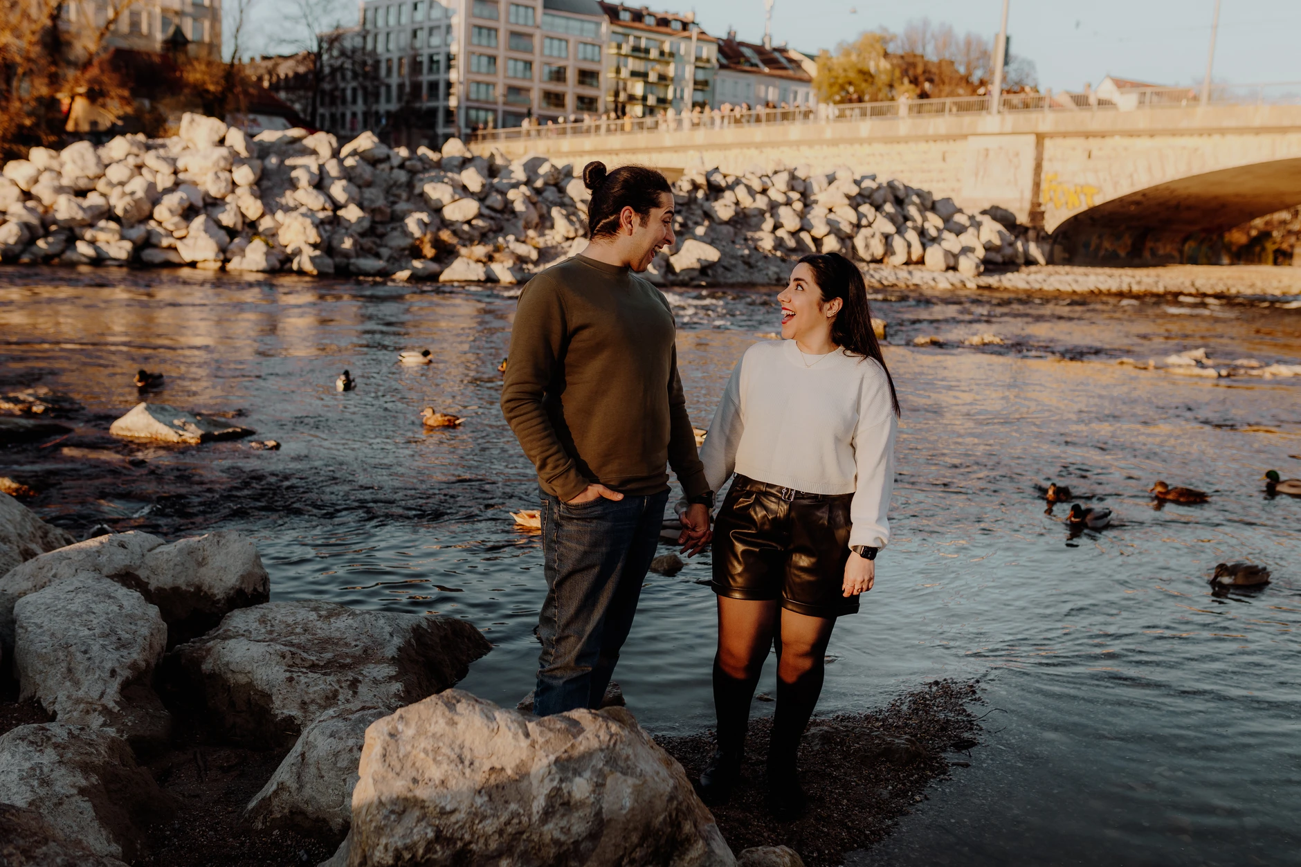 Couple standing together at the water's edge in front of winter trees