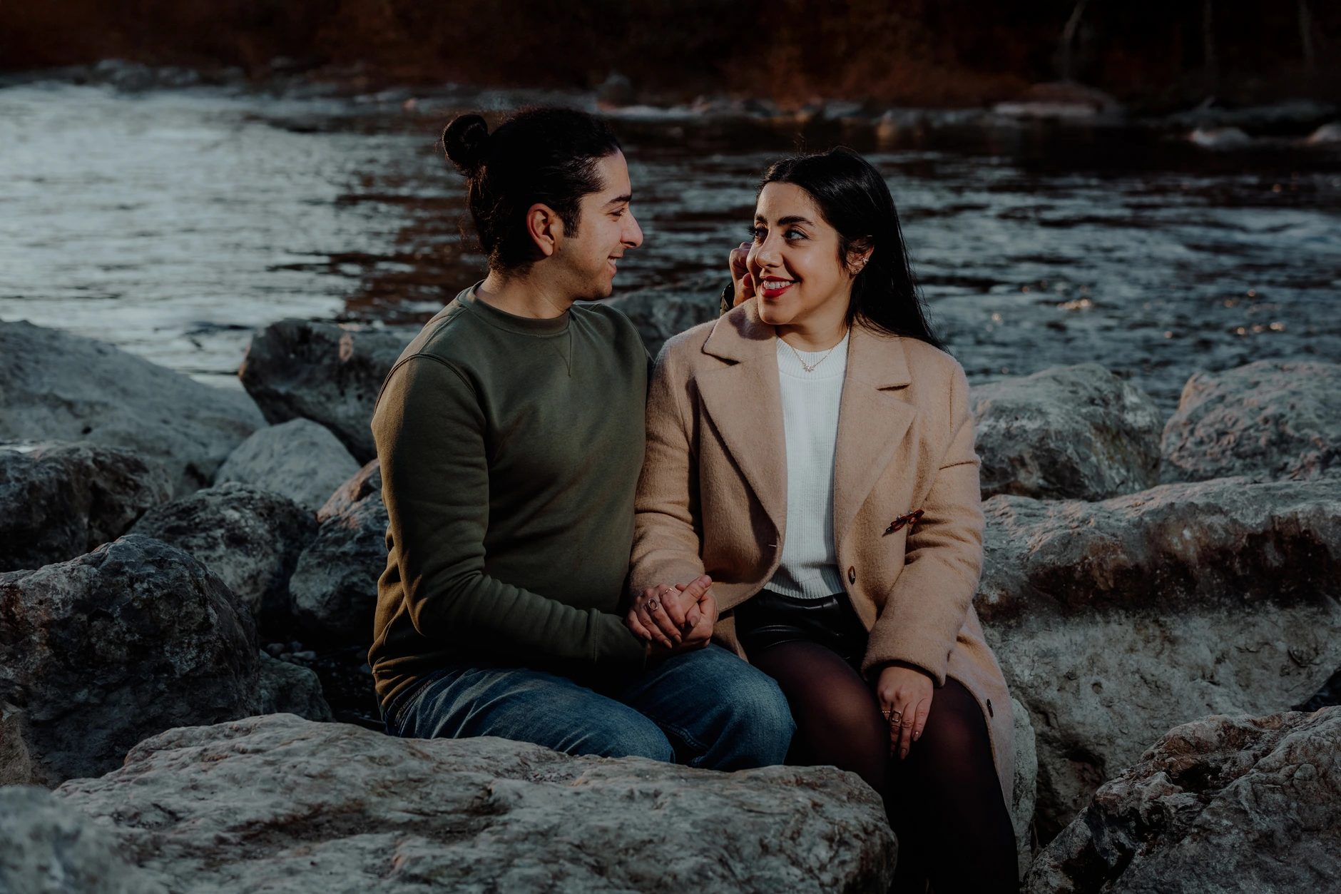 Couple sitting relaxed on boulders by the riverside