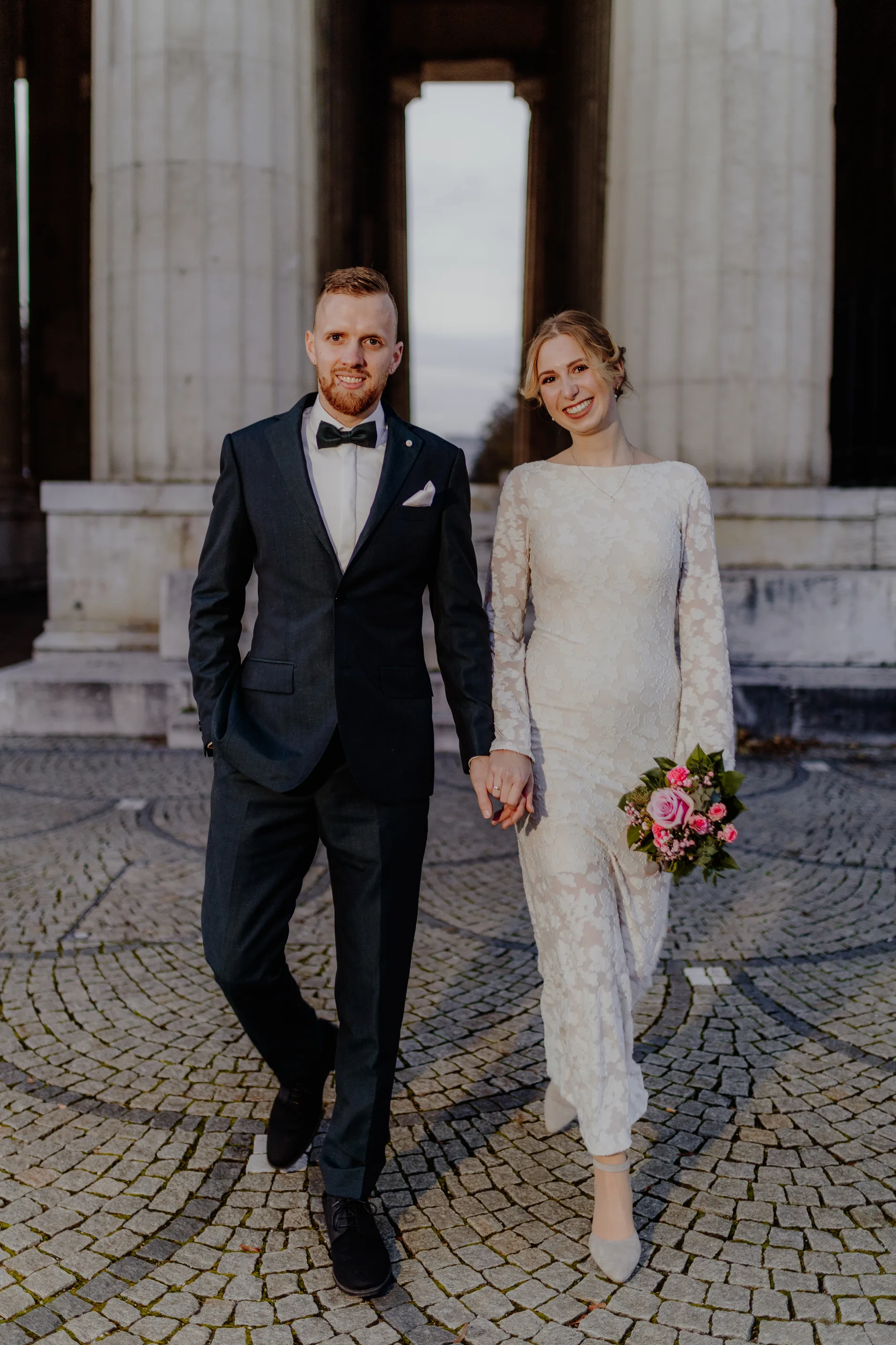 Couple walking hand in hand in front of the columns at Königsplatz