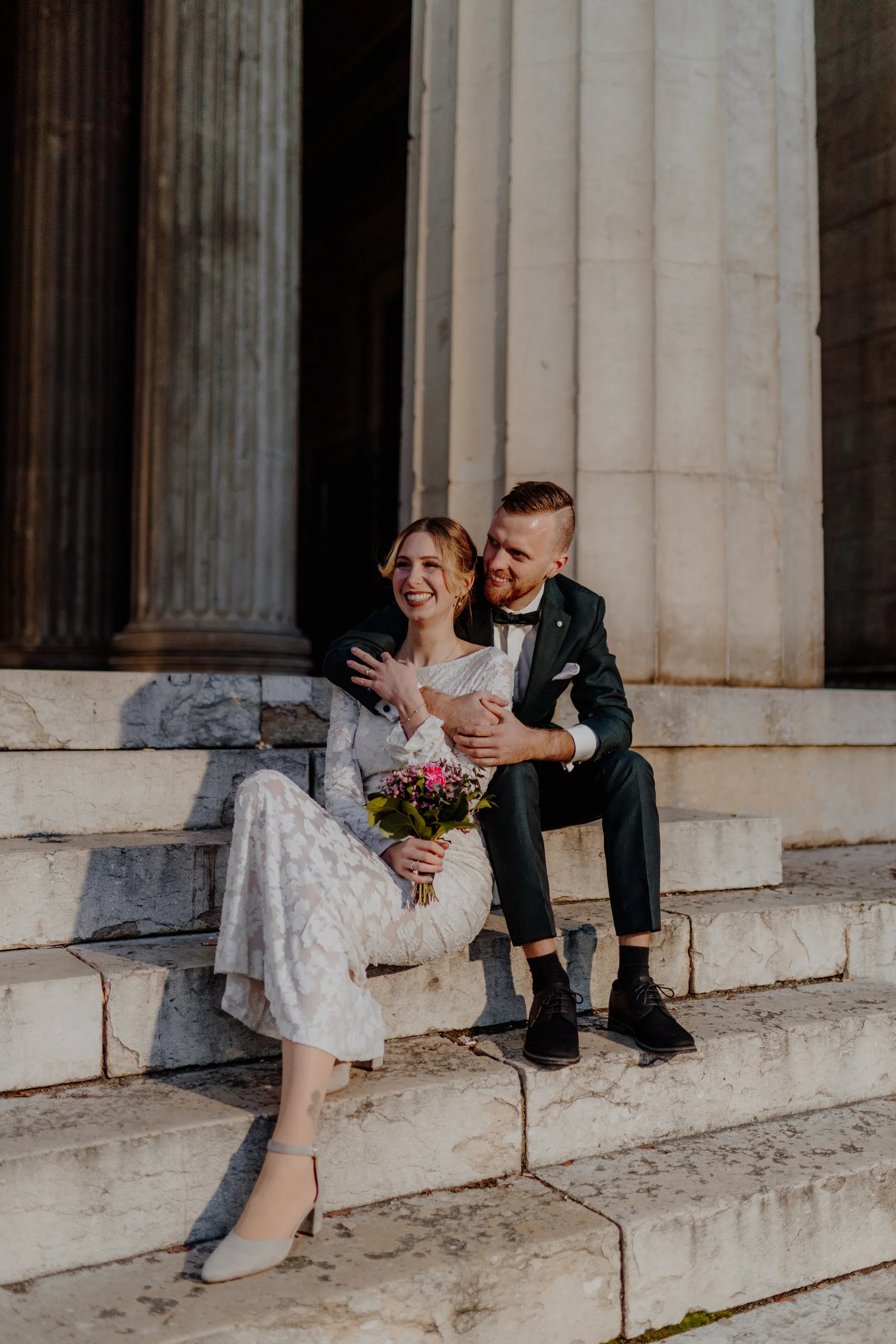 Bride in white dress, groom in tailored suit — neoclassical backdrop